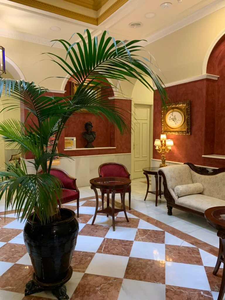 Diagonal floor tiles (brown and white) and a large palm in a pot welcome you to the reception of a hotel in Seville Spain.