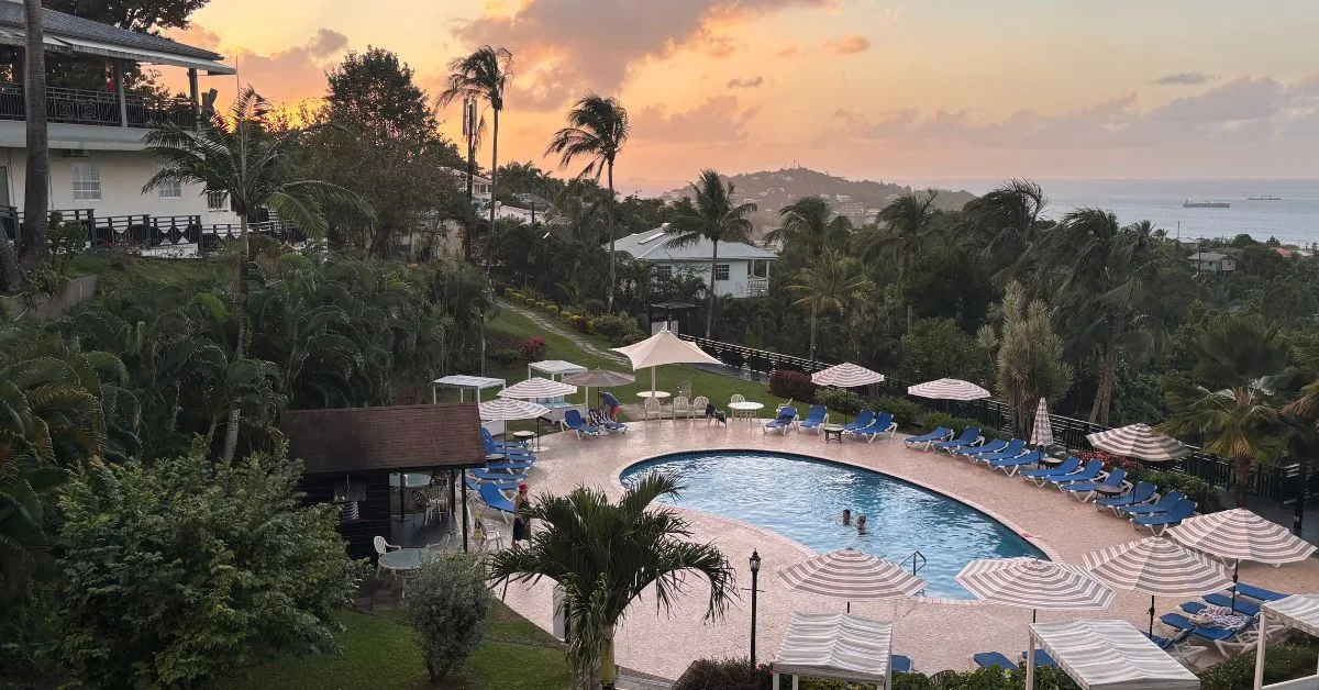 Hotel in the evening with the sunset in the background and the pool and sun loungers in the foreground. Palm trees around the pool area.