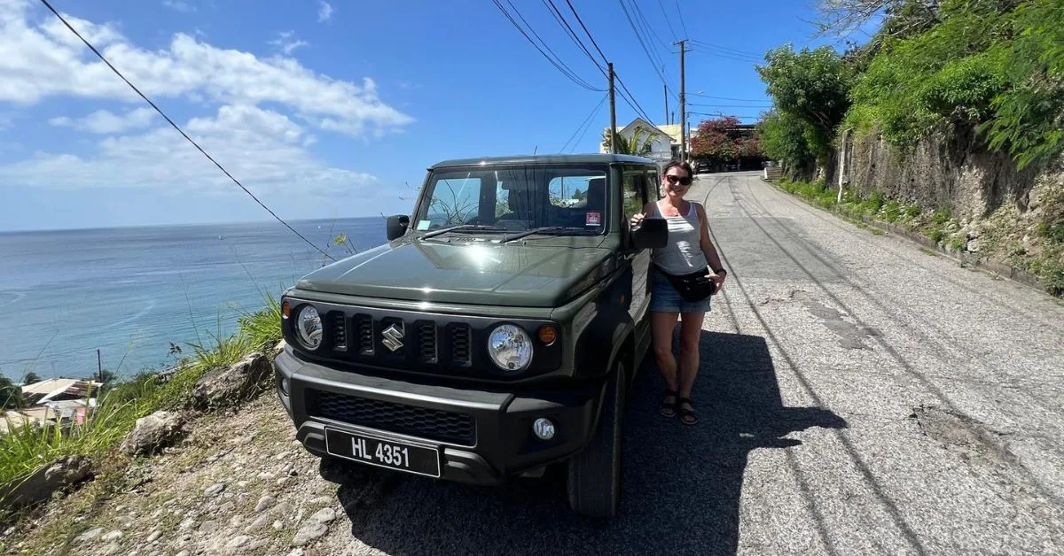 Woman standing next to a green jeep on a minor road in St Lucia with the sea in the background.