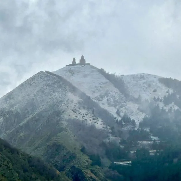 Snow-capped mountain with a small ancient church/monastery on top.