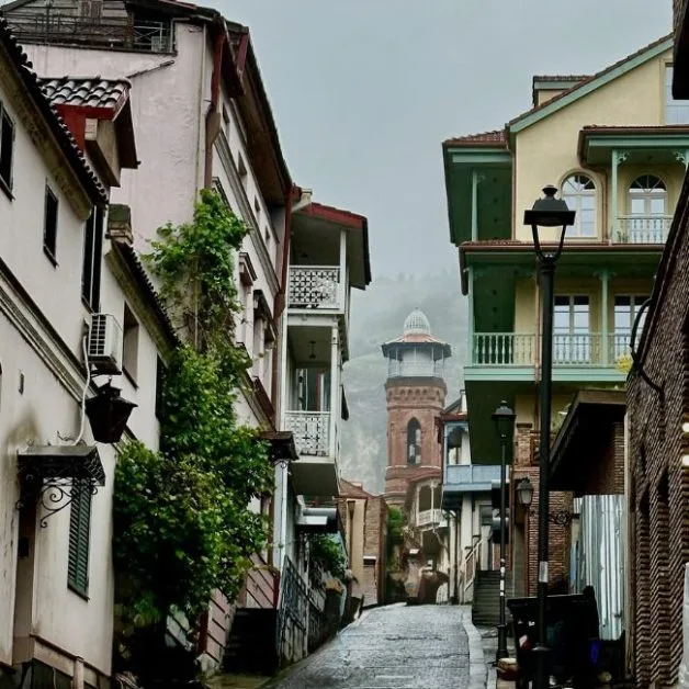 Old Tbilisi cobbled street with homes at either side of the narrow street and a church  tower at the end of the street.
