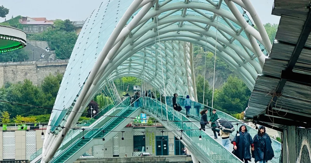 People cross a covered glass arched bridge in Tbilisi Georgia.