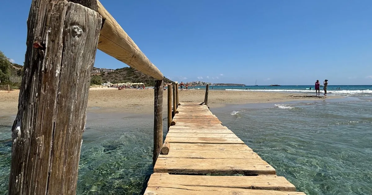 A wooden boardwalk to a beach on the island of Crete, Greece. People walking on a sandy beach.