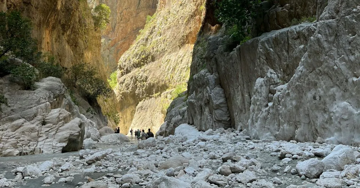 People walking through a gorge rock area on the island of Crete. Large boulders are scattered on the floor of the gorge.