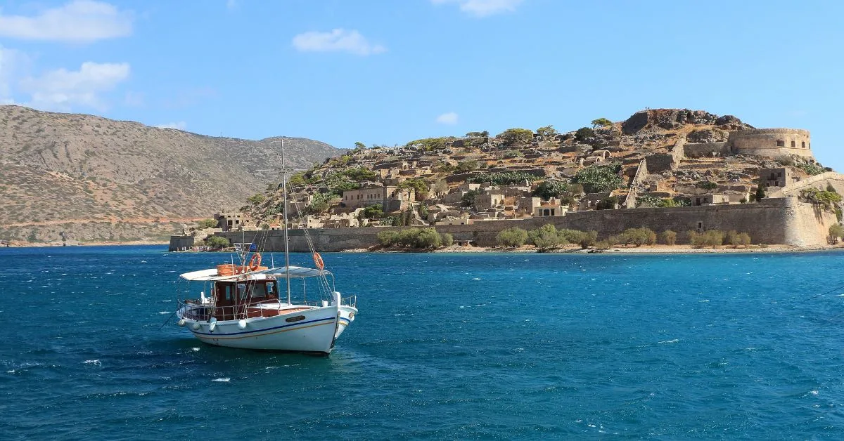 A small boat sitting just offshore from the Greek island of Spinalonga where building are carved out of the rock.