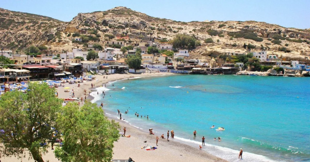 Homes, shops and restaurants around a sandy bay on Crete.