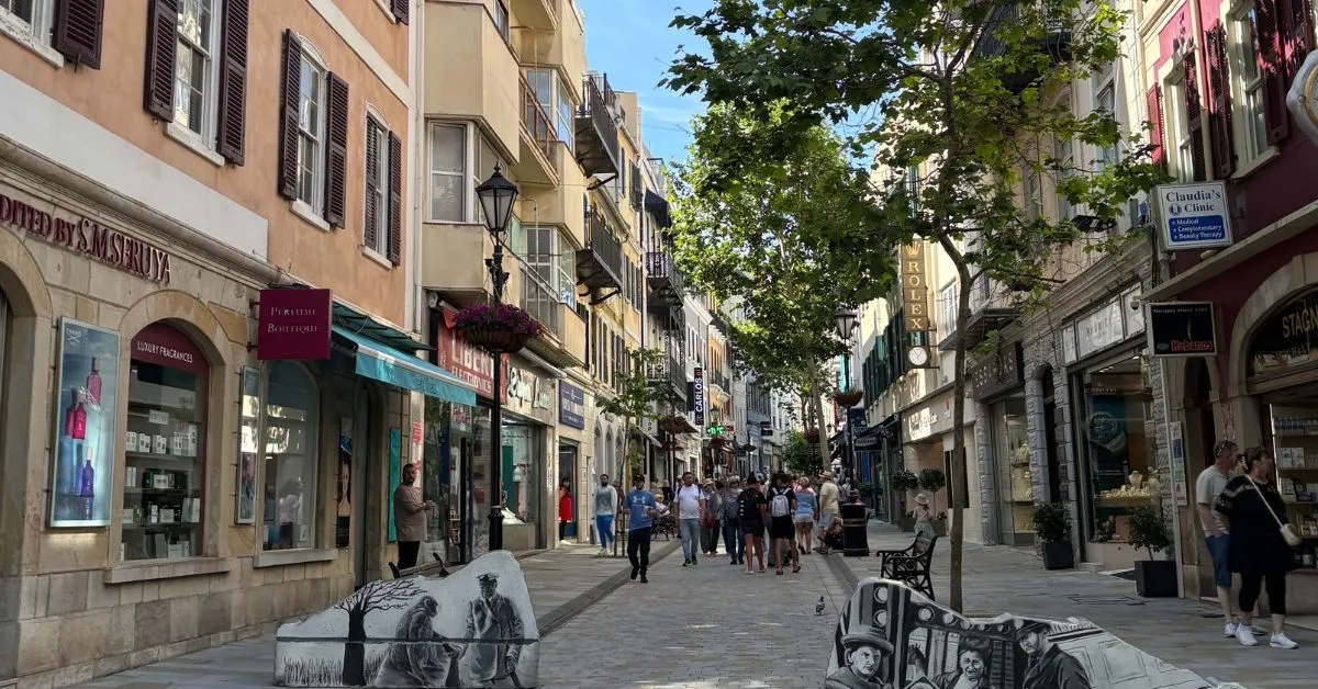 Pedestrianised street in Gibraltar. Daytime so people walking along the street. Shops either side of walkway.
