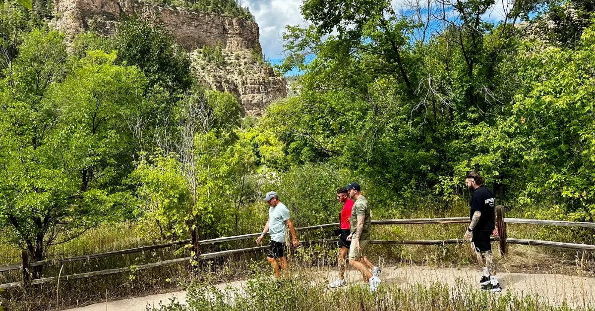 People hiking a trail which is surrounded by trees and canyon cliffs.
