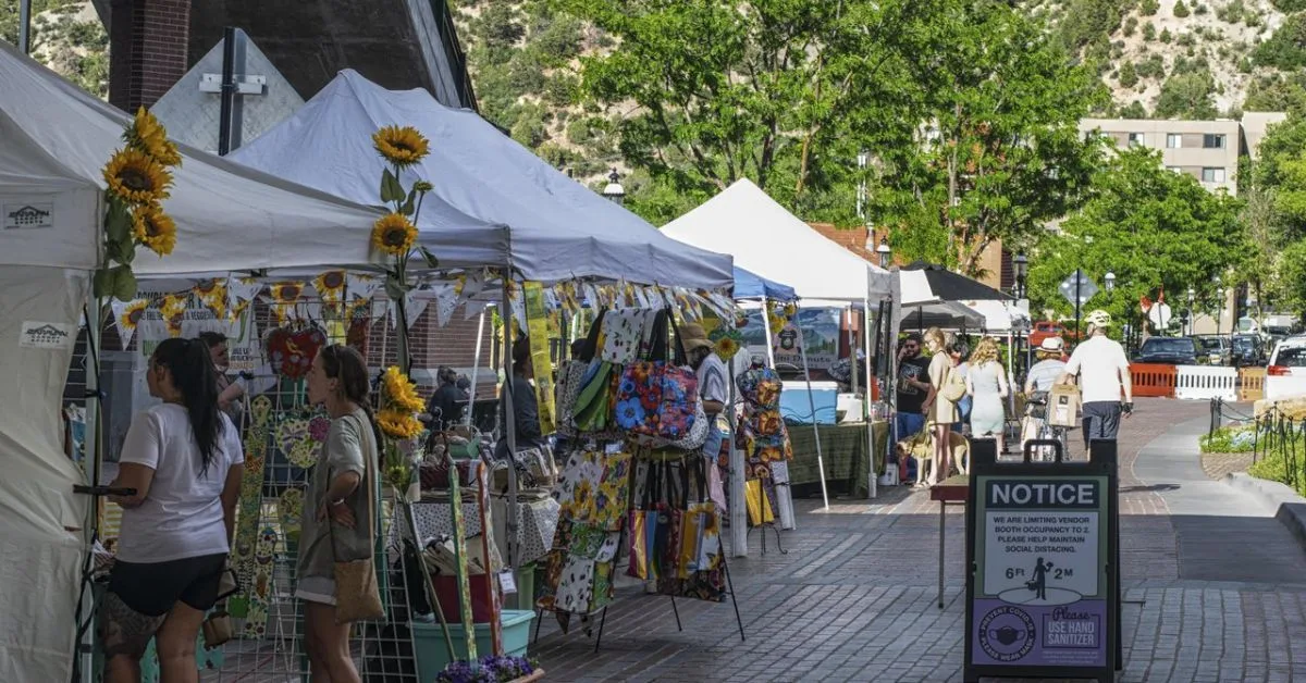 Visitors are browsing a street of arts and craft stalls under white canopy tents.