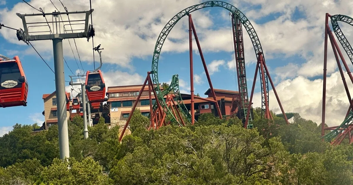 Mountain top roller coaster with loops and behind it a building with restaurant and other entertainment for visitors.