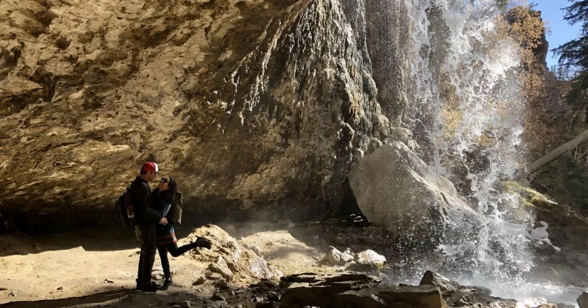 Two people admiring the waterfalls at Hanging Lake where water is rushing over the 'edge' of a cliff.