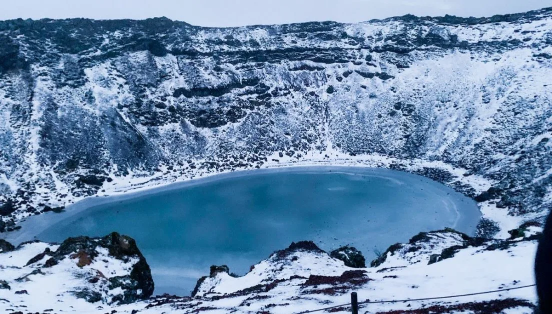 A large blue lake with ice and steep rock inc
