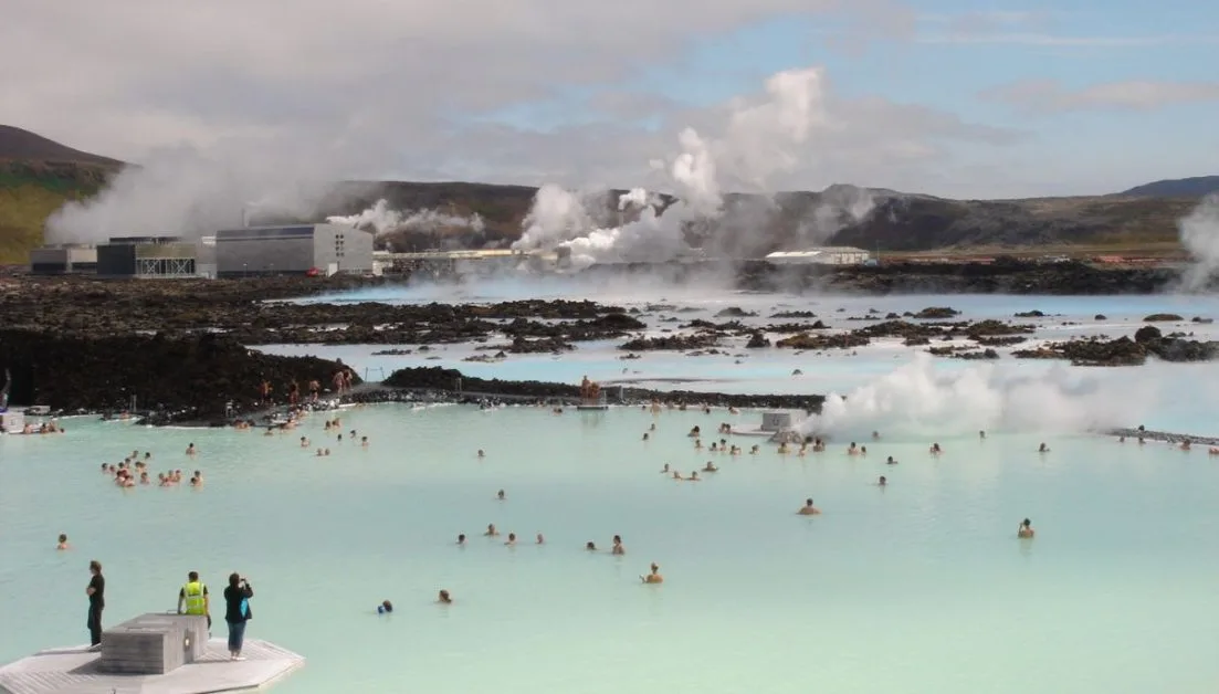 Large area of hot spring pools with steam coming from them. Lots of people in the water.