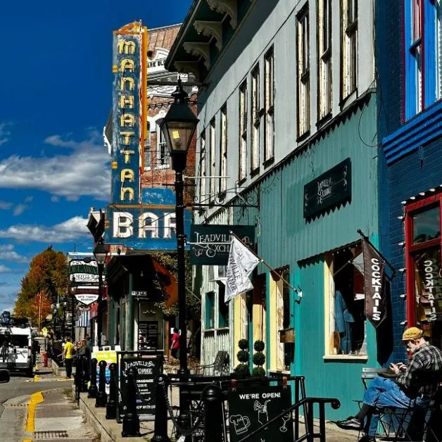 Leadville Co Harrison Street with outdoor seating and signs for a bar and other shops hanging out from the buildings. Building are painted different colours from dark blue to lighter blue and yellow.