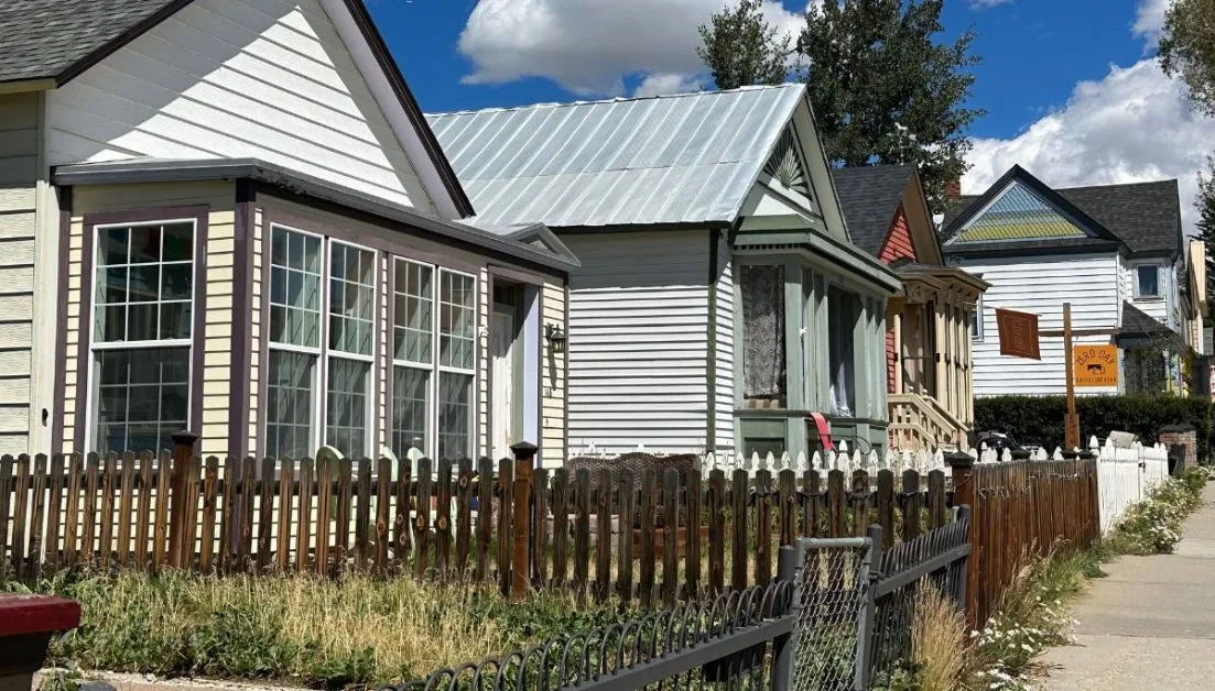 Street with 1 story original Leadville homes. each is painted a different colour and all have a wooden or iron fence.
