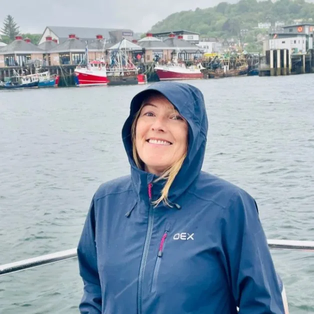 Woman on a boat coming into the Oban harbour where fishing boats ae moored.
