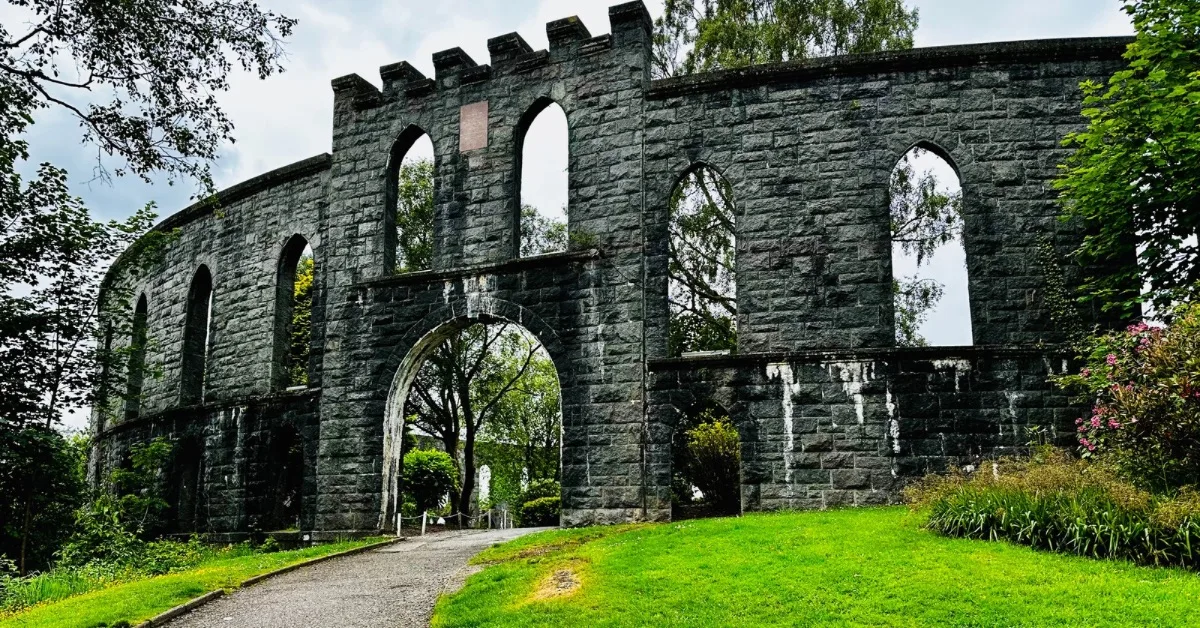 A large grey stone circular arched structure with grass lawns and shrubs around it.