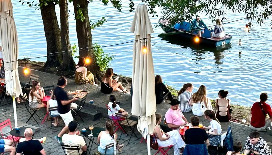 Waterside tables and chairs and people boating in the river in Prague.