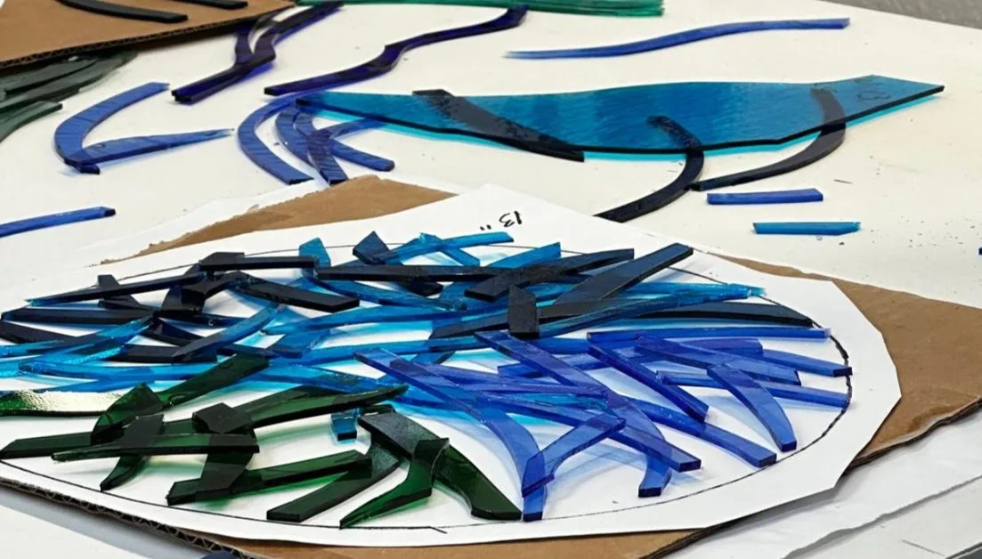 Glass pieces in green and blue are laid out on a cardboard template ahead of fusing them. Glass fusing Classes are on offer in Sarasota.