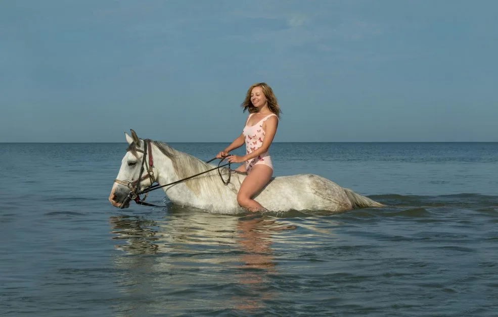 A unique thing to do in Sarasota is to ride a horse on the beach and in the shallow warm waters. A woman is enjoying riding her horse in the water.