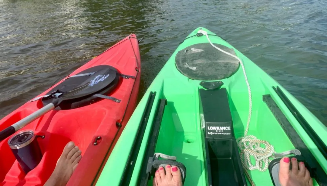 Two kayaks on the water, one is green and the other red. They are in Sarasota Bay enjoying paddling calm waters.