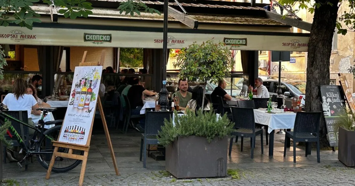 Skopski Merat restaurant with outdoor tables and people sitting eating. Trees and plants add a relaxed feel to this part of Skopje.