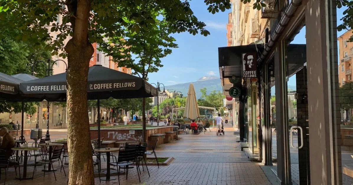 Main pedestrian street with cafe seating, trees and a few people strolling or sitting enjoying coffee.