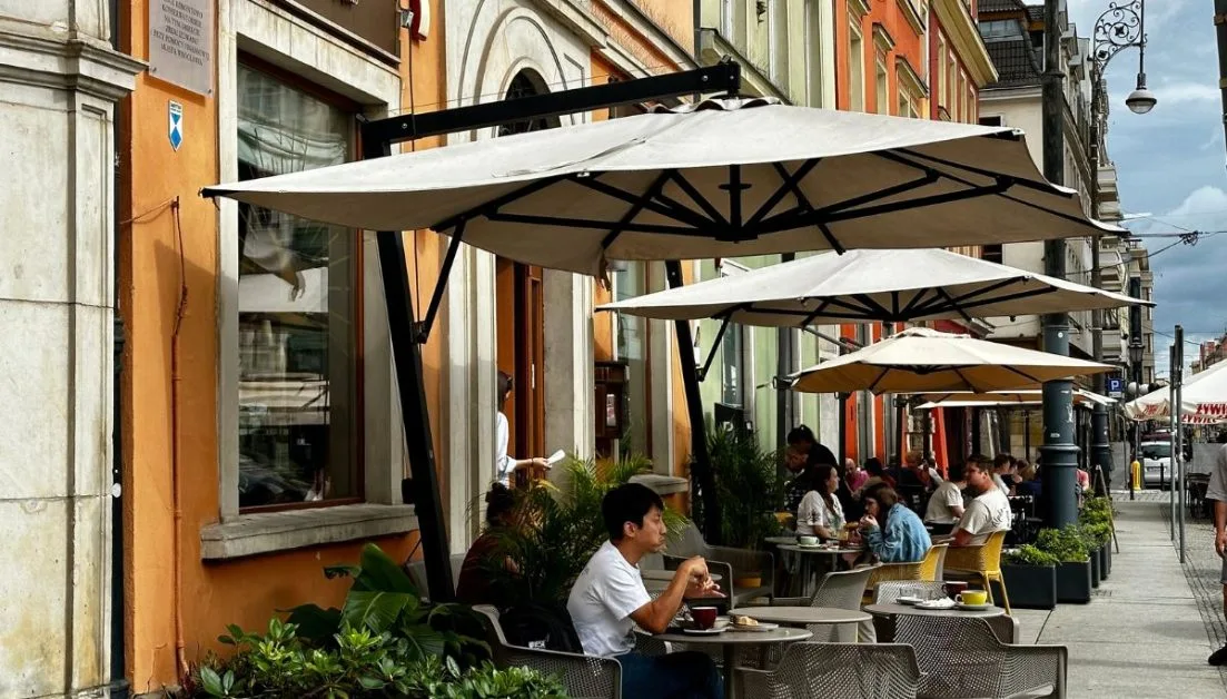 People sitting under umbrellas enjoying breakfast in Salt Square, Wroclaw.