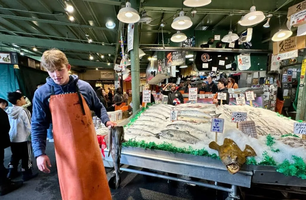 Fish Market in Seattle. A man is standing next to stall with one of the fish for sale in his hand.
