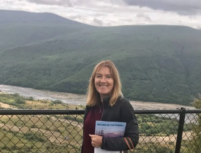 Woman at Mount st Helens Visitor Center holding a brochure. In the background are mountains.