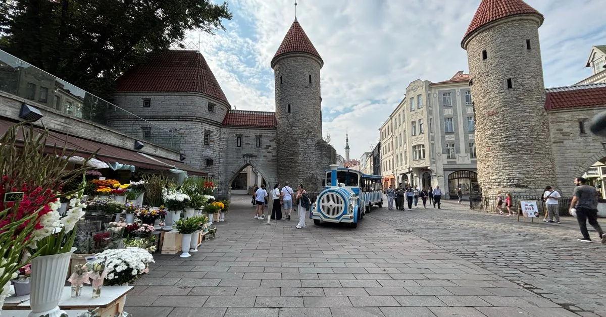 Two stone pillars show entrance to Tallinn Old Town with a flower market to the left of the images