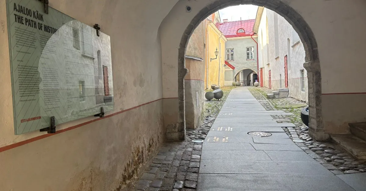 Entrance to Path of History showing narrow paved stones with dates on them leading through an archway and then continuing to the end of the walkway