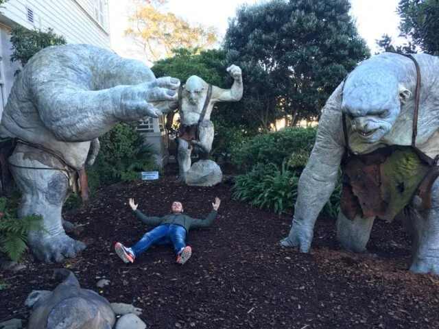 A man is lying between larger than life replicas of characters from Lord of the Rings. The films were partially filmed in this location in New Zealand