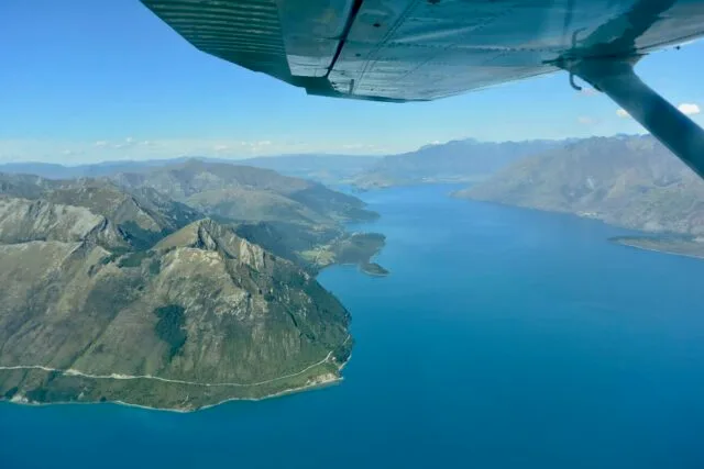 Fjords and mountains visible from a small plane. A small part of the wing of the plane is visible.