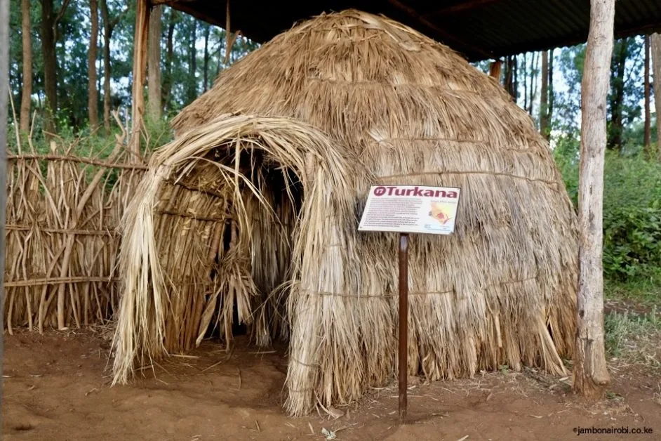A straw hut with a rounded roof and an arch entryway. It is part of a display of traditional Kenyan homes.