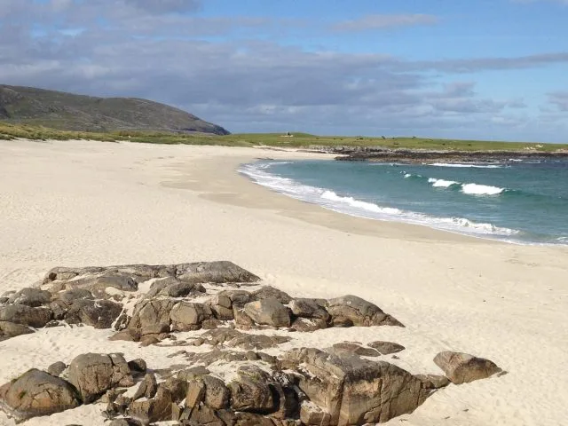 Remote beaches with white sands and blue waters lapping the shore. Large rocks lay on part of the beach.
