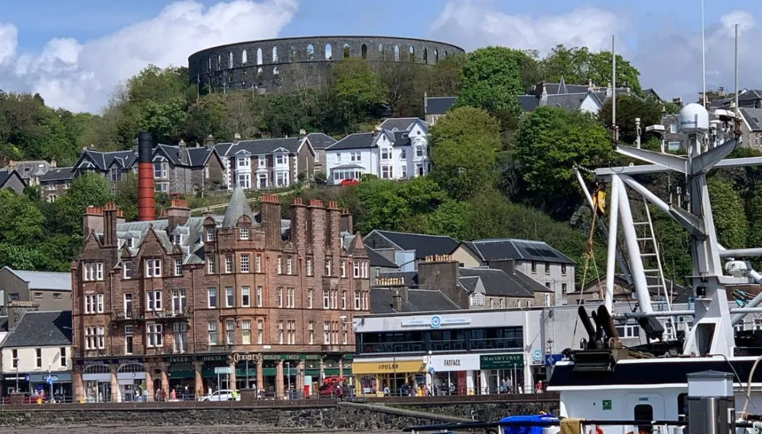 Round stone tower on a hill above the slate roofed buildings of the Scottish town of Oban.