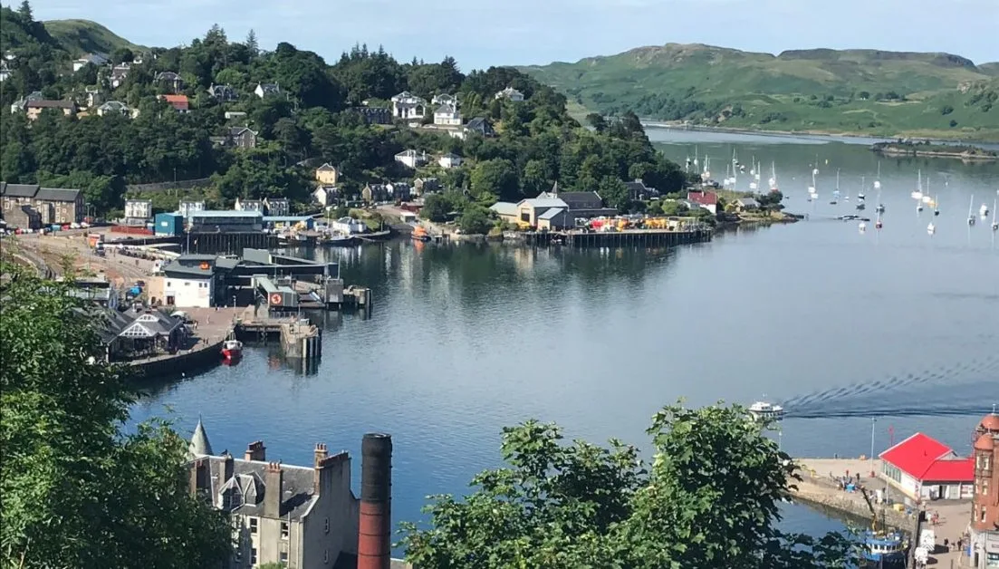 A view over the bay of Oban in Scotland with small boats anchored and a harbour area where larger ferries dock.