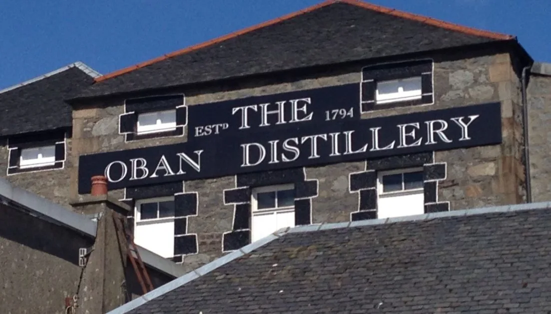 A large black and white Oban Distillery sign above the malt whisky production building entrance in the town of Oban, Scotland.