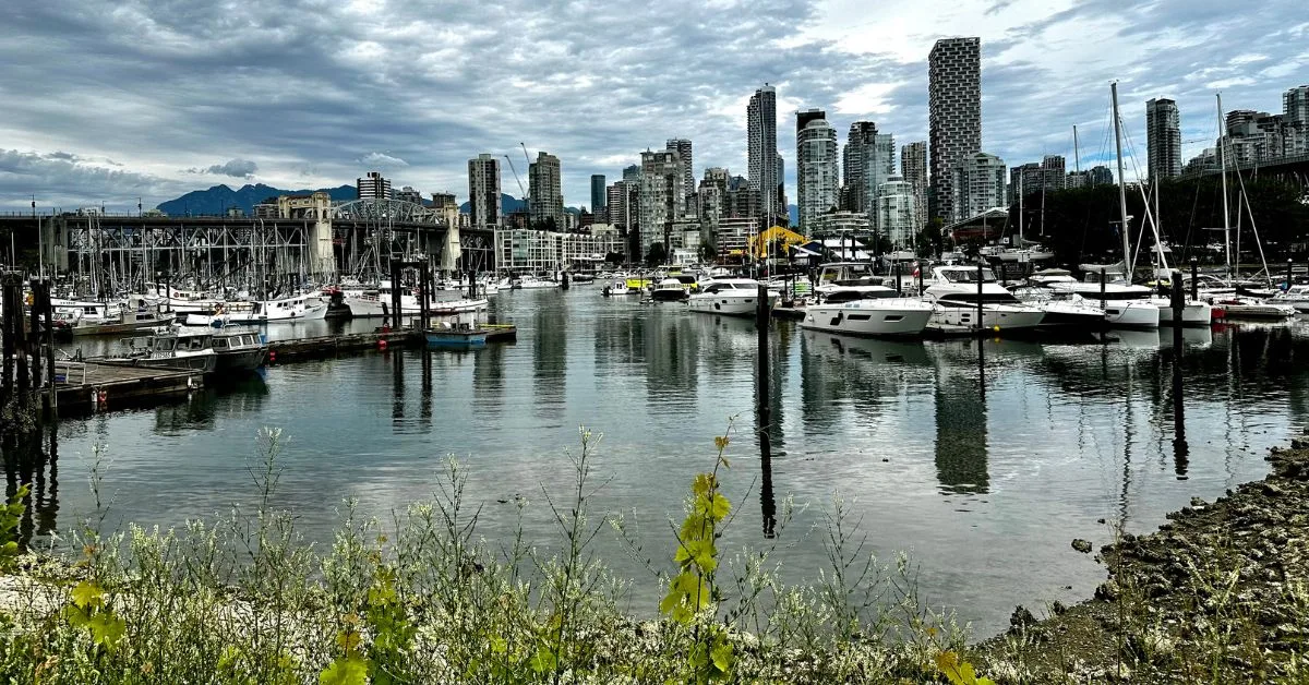 A view of Vancouver, Canada city from boat harbour. Multi story skyline and behind are mountain peaks.  Small boats anchored in the harbour.
