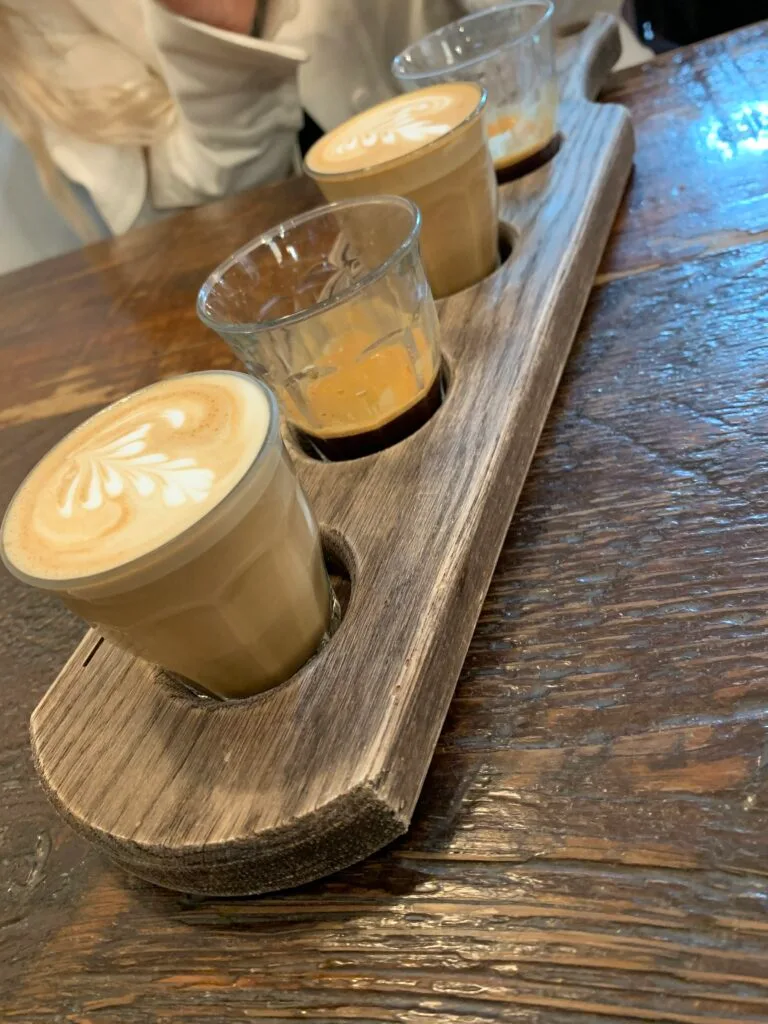 Four glass cups of coffee served on a wooden tray.