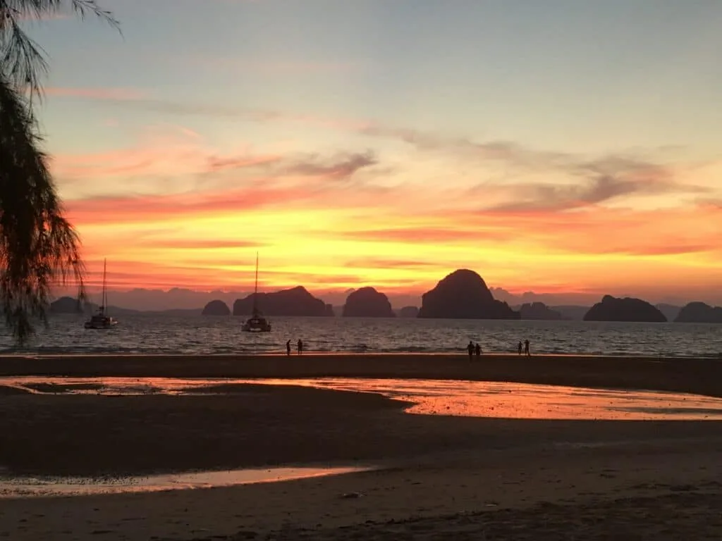 Orange sky Sunset over coastal rocks with boats moored in the bay and people walking on the beach.