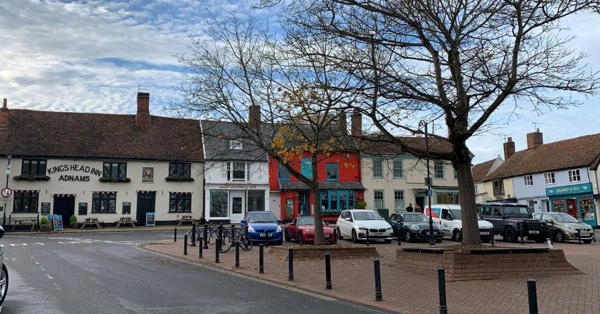 A bricked square area in Woodbridge with cars parked and several restaurants and shops behind. The area also is where a farmers market is held.