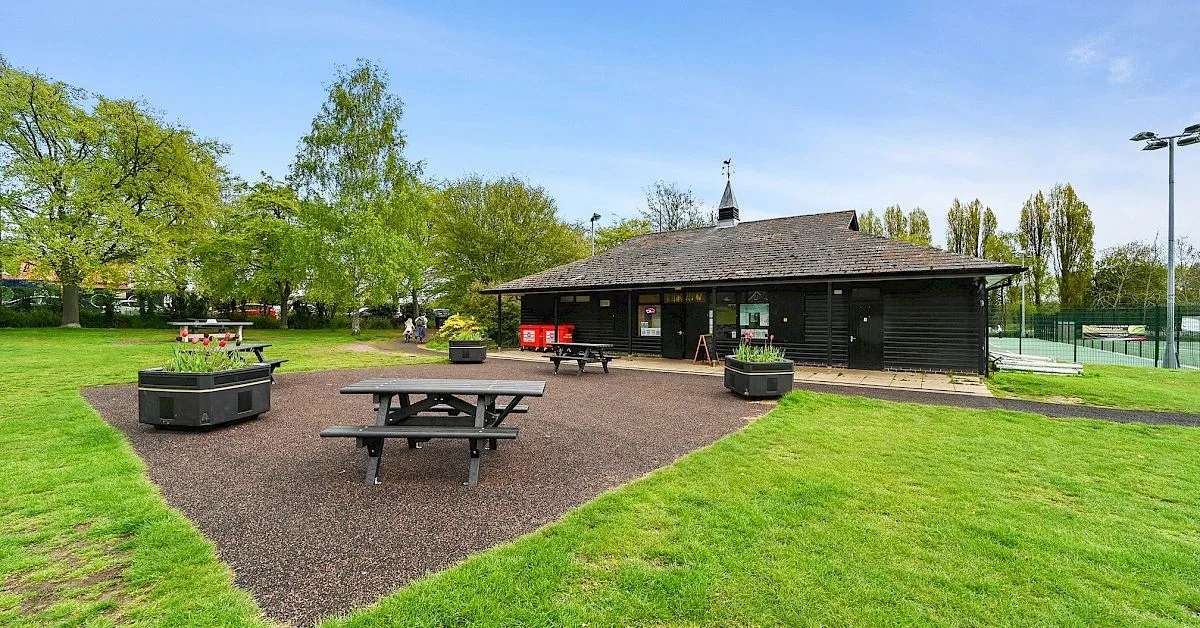 Picnic tables in a garden area surrounded by grass lawns.  Also the  Tea Hut where you can enjoy a break during a visit to one of the public parks in Woodbridge.