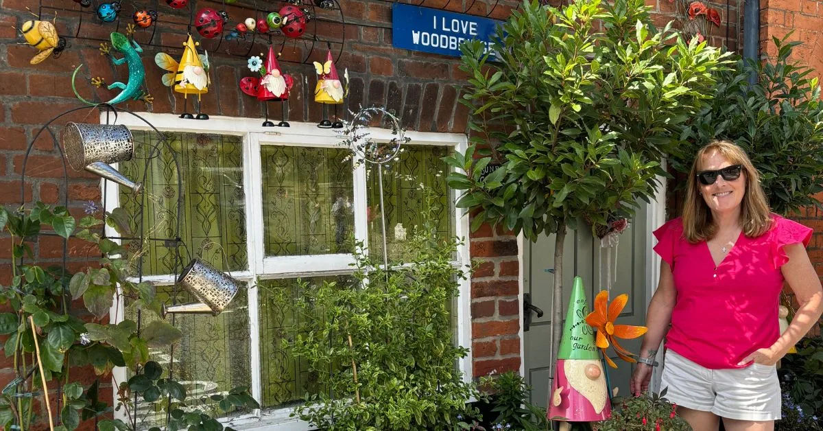 Travel Blogger Jude outside a red brick cottage in Woodbridge. The front is highly decorated with garden decor including gnomes and ladybirds attached to the brick.