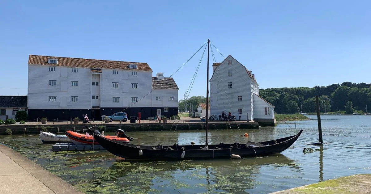 Tide Mill in Woodbridge is an operating floor mill.  A long boat is moored in the quayside in front.