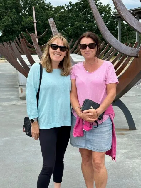 Travel Bloggers Jude and Ruby visiting Sutton Hoo Suffolk and are standing in front of a medieval boat replica.