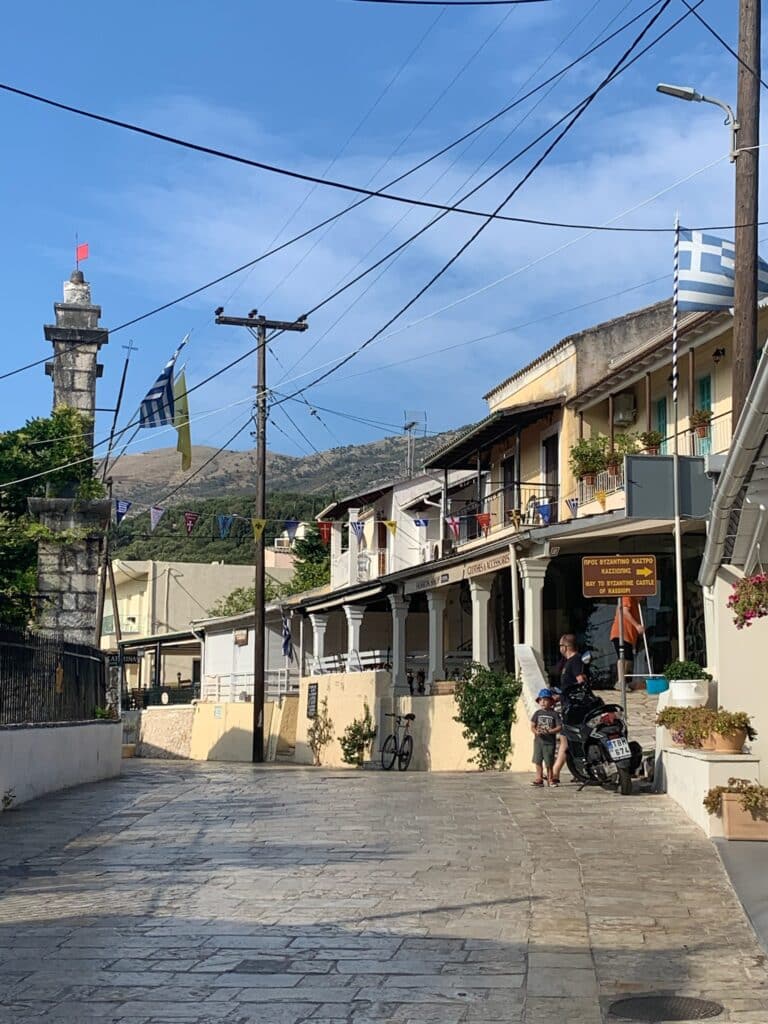 Cobbled street with various buildings and a church steeple. Wires criss cross the sides of the street.