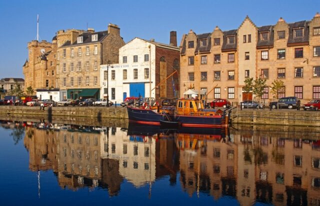 A row of buildings in Edinburgh is reflected in the calm waters of Leith.