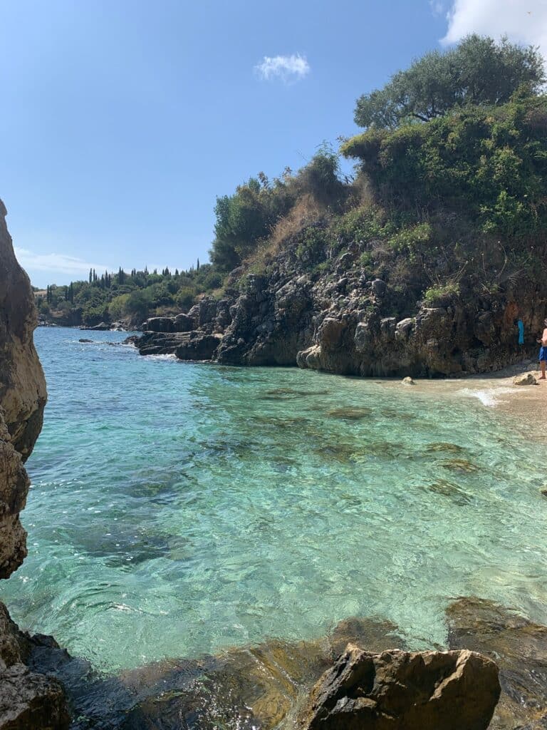 A small cove with beach and rocks, edged with trees that fridge the water's edge.
